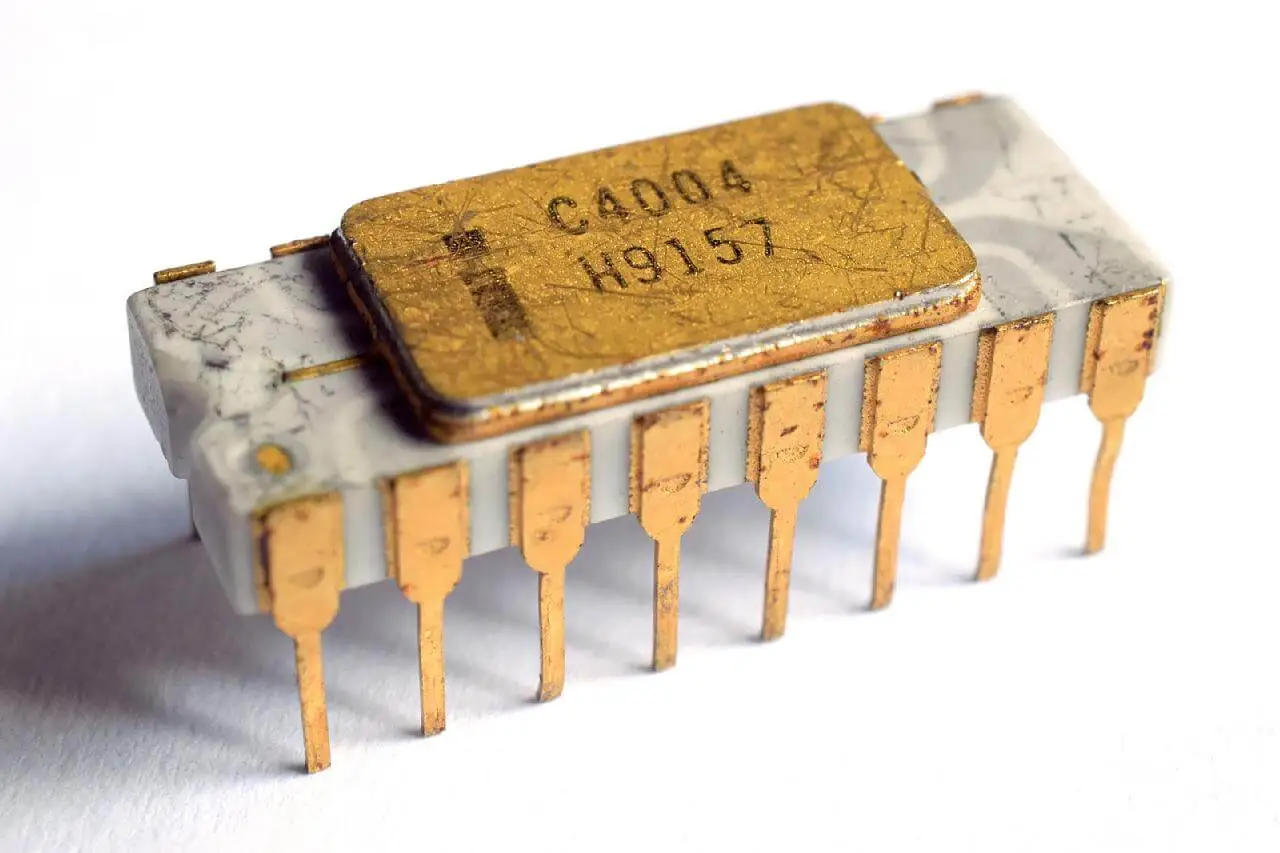 A closeup image of the Intel 4004 processor, with the original gold-plated pins and grey ceramic body.